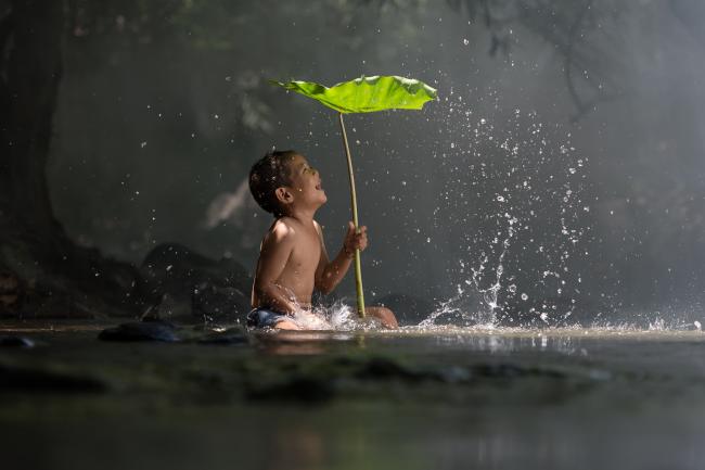 Enfant sous une feuille jouant avec de l'eau en Asie